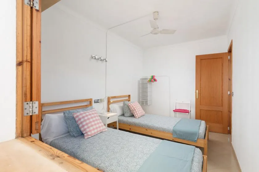 A bright bedroom with two single beds and a ceiling fan.
