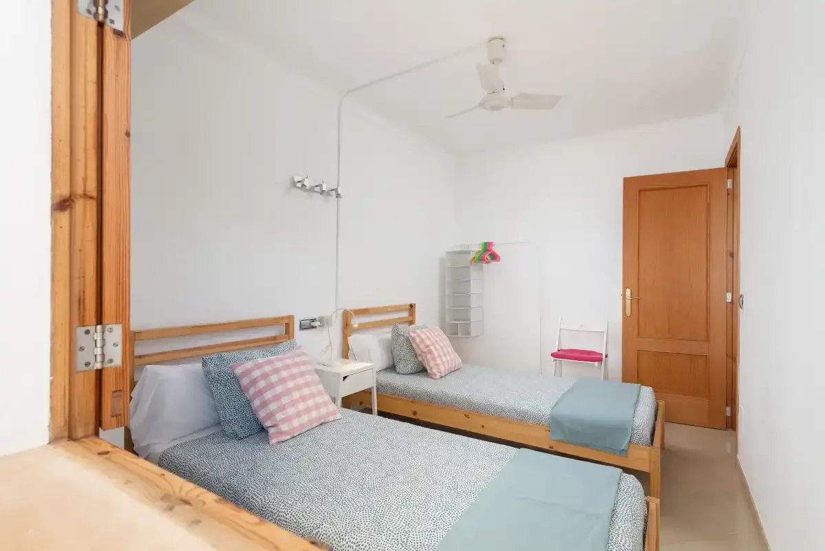 A bright bedroom with two beds and a ceiling fan.