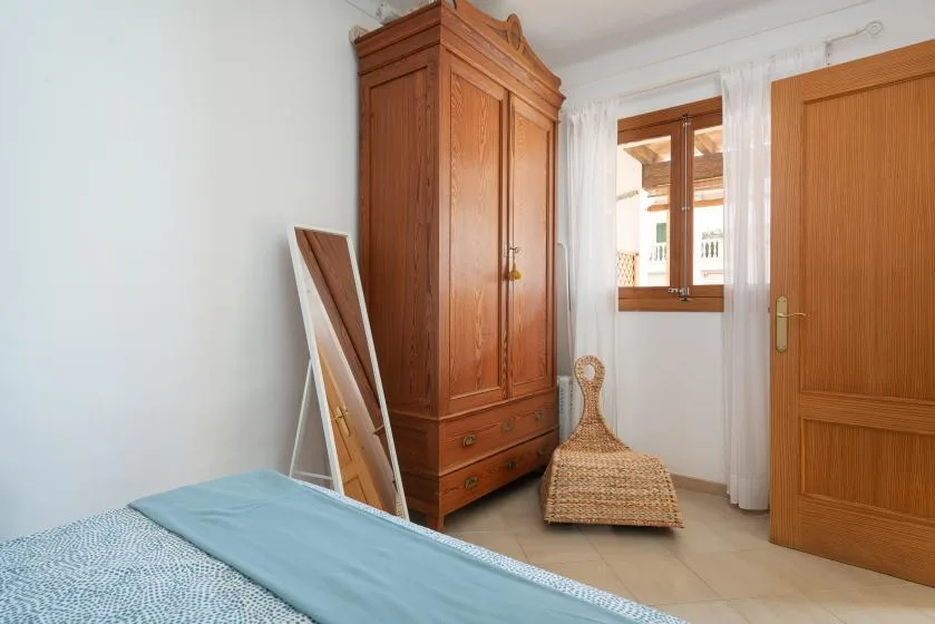 A bedroom with a wooden wardrobe beside a bed and window.