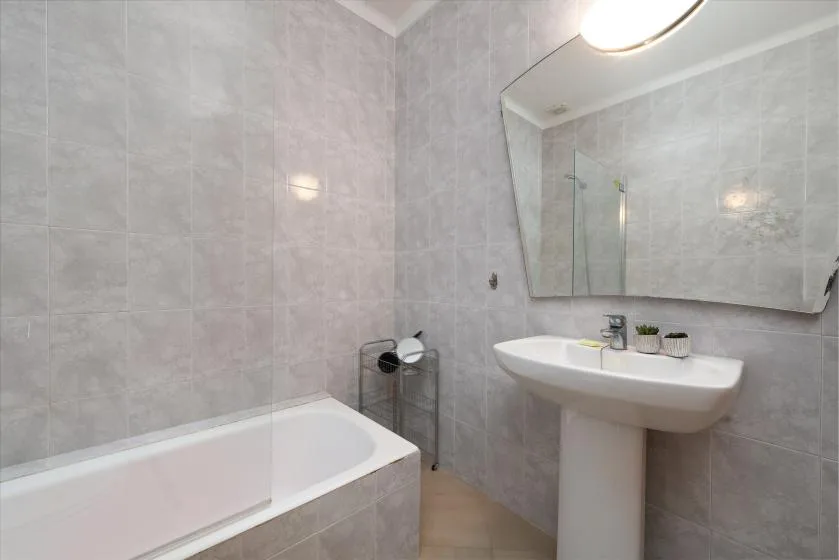 A tiled bathroom with a bathtub and a pedestal sink beneath a large mirror.
