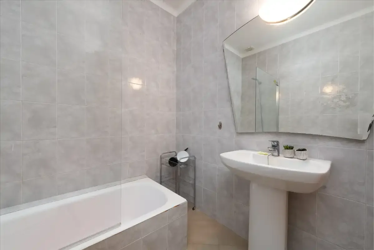 A tiled bathroom with a bathtub, sink, and large wall mirror.