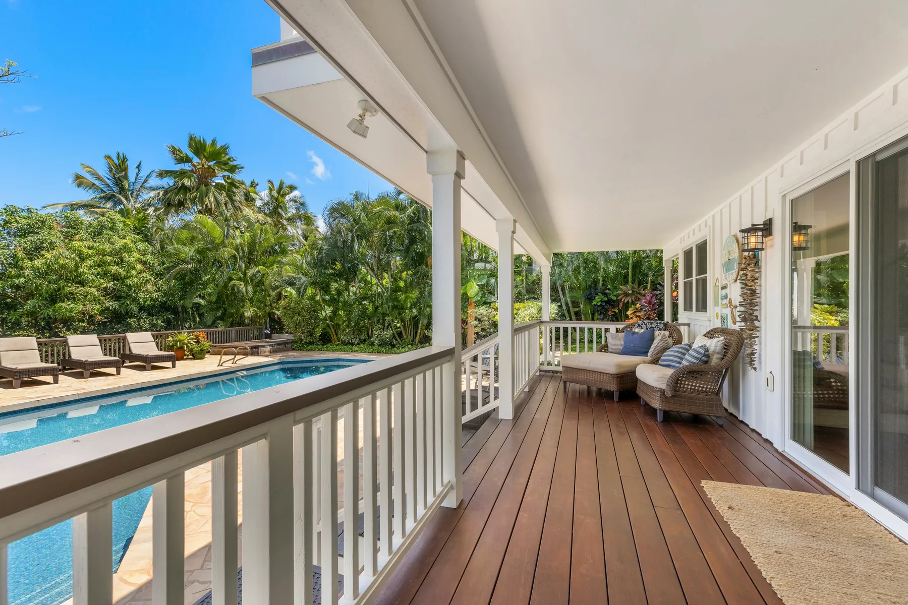 Covered deck seating overlooks a swimming pool and tropical greenery.