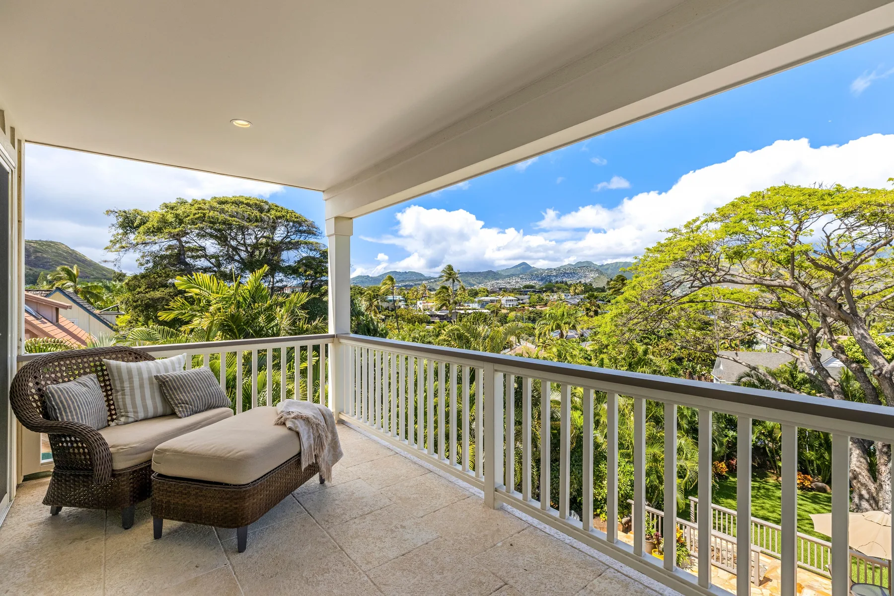 A covered balcony with cushioned seating overlooks leafy trees and distant mountains.