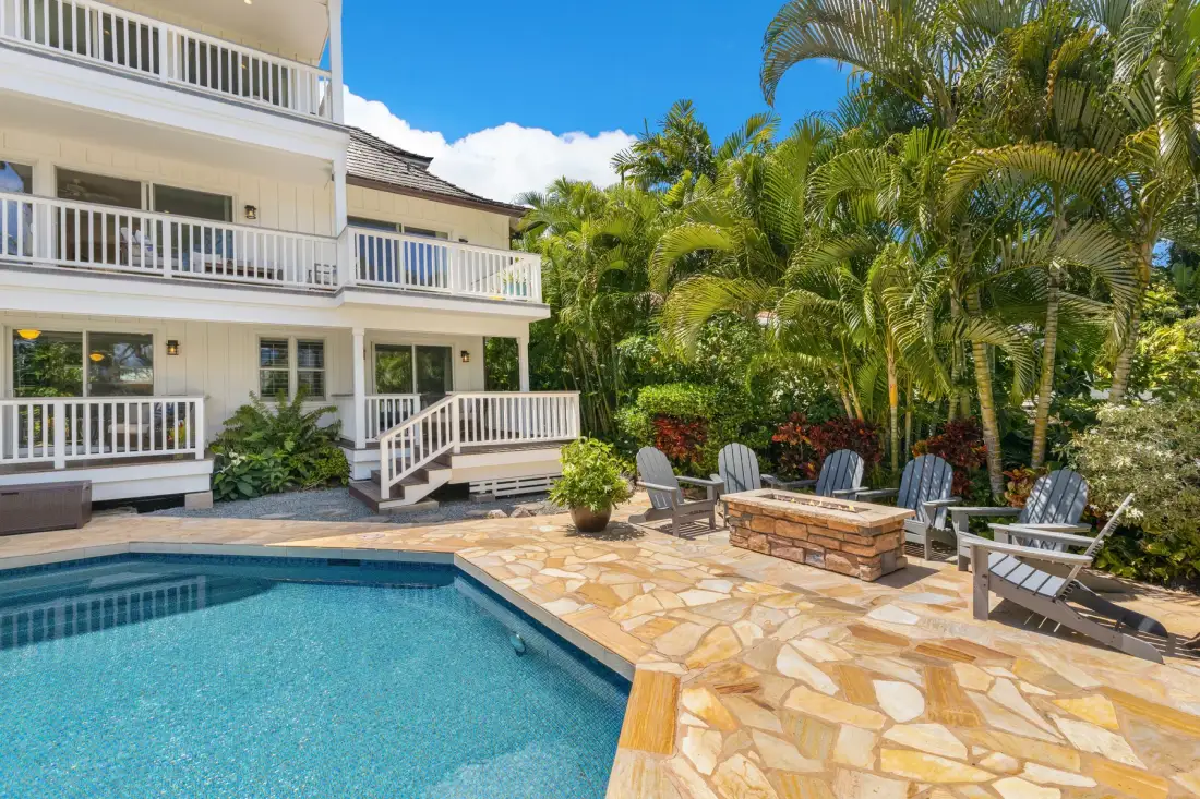 A poolside patio beside a white multi-story building, with palms and outdoor seating.