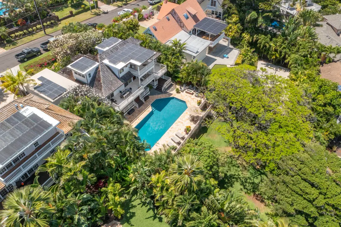 An aerial view shows homes, a turquoise swimming pool, and surrounding greenery.