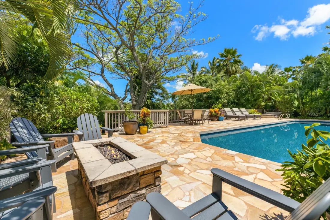 An outdoor swimming pool is surrounded by a stone patio and lounge seating.