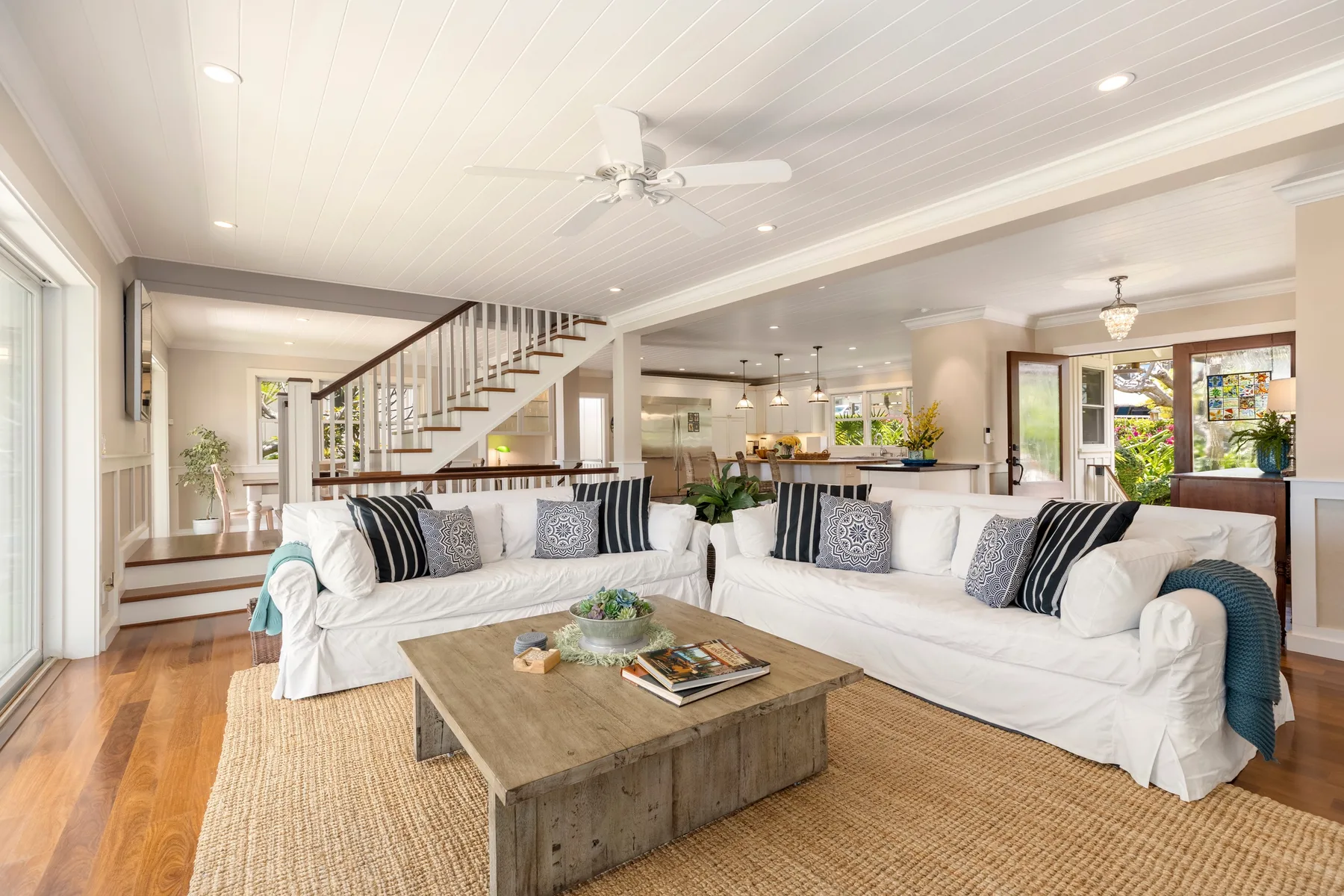 A bright living room with white seating, a coffee table, and a staircase.