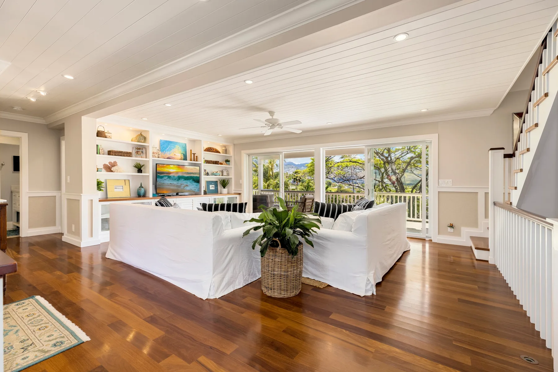 A bright living room with white seating, built-in shelves, and large windows.