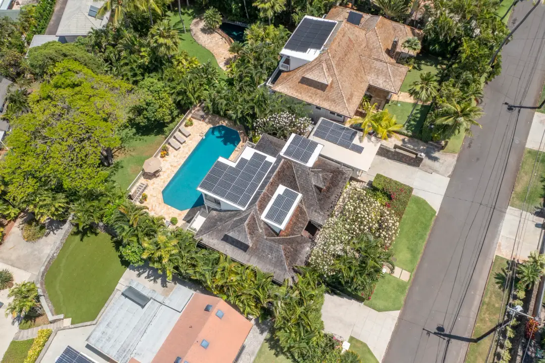 An aerial view of a house with rooftop solar panels beside a swimming pool.