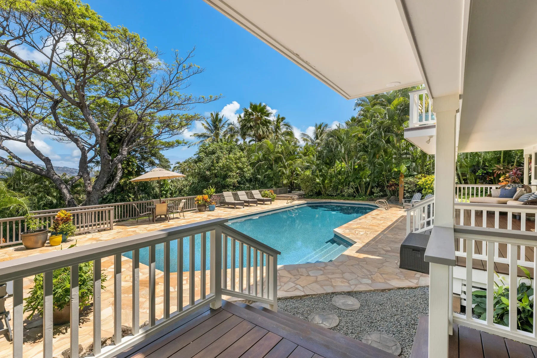 A pool patio with surrounding greenery and a shaded seating area.