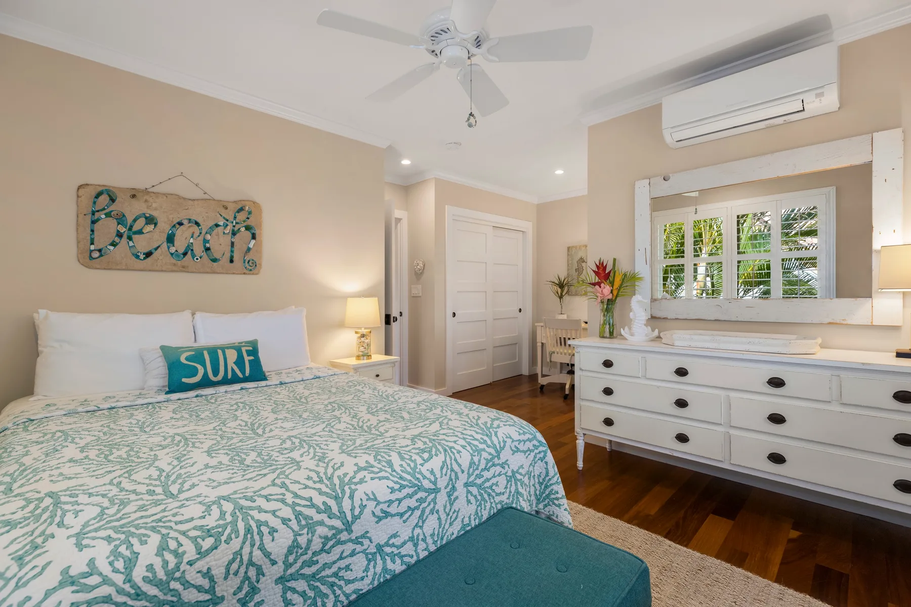 A bedroom with a bed dressed in a turquoise patterned cover and a white dresser.