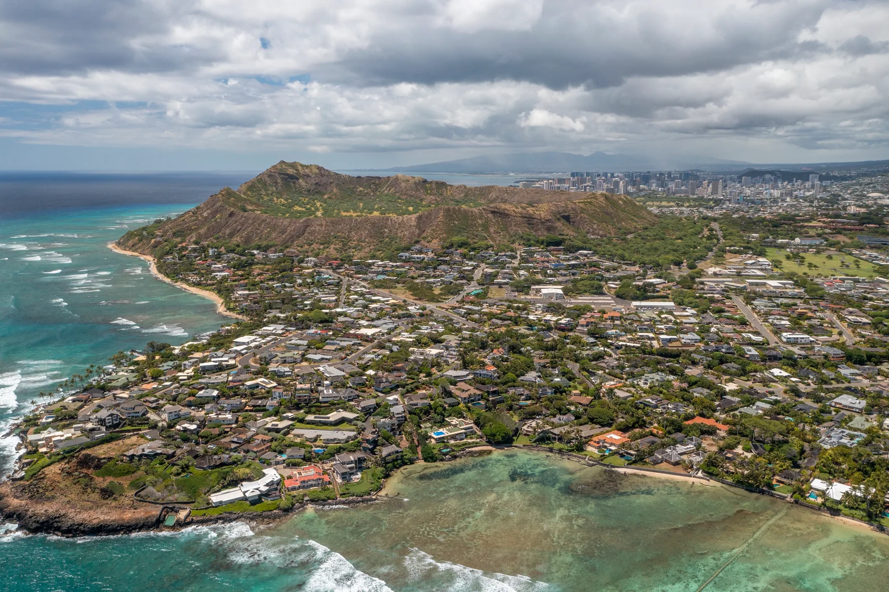 Aerial view of a coastal neighborhood, with a green ridge beside the ocean.