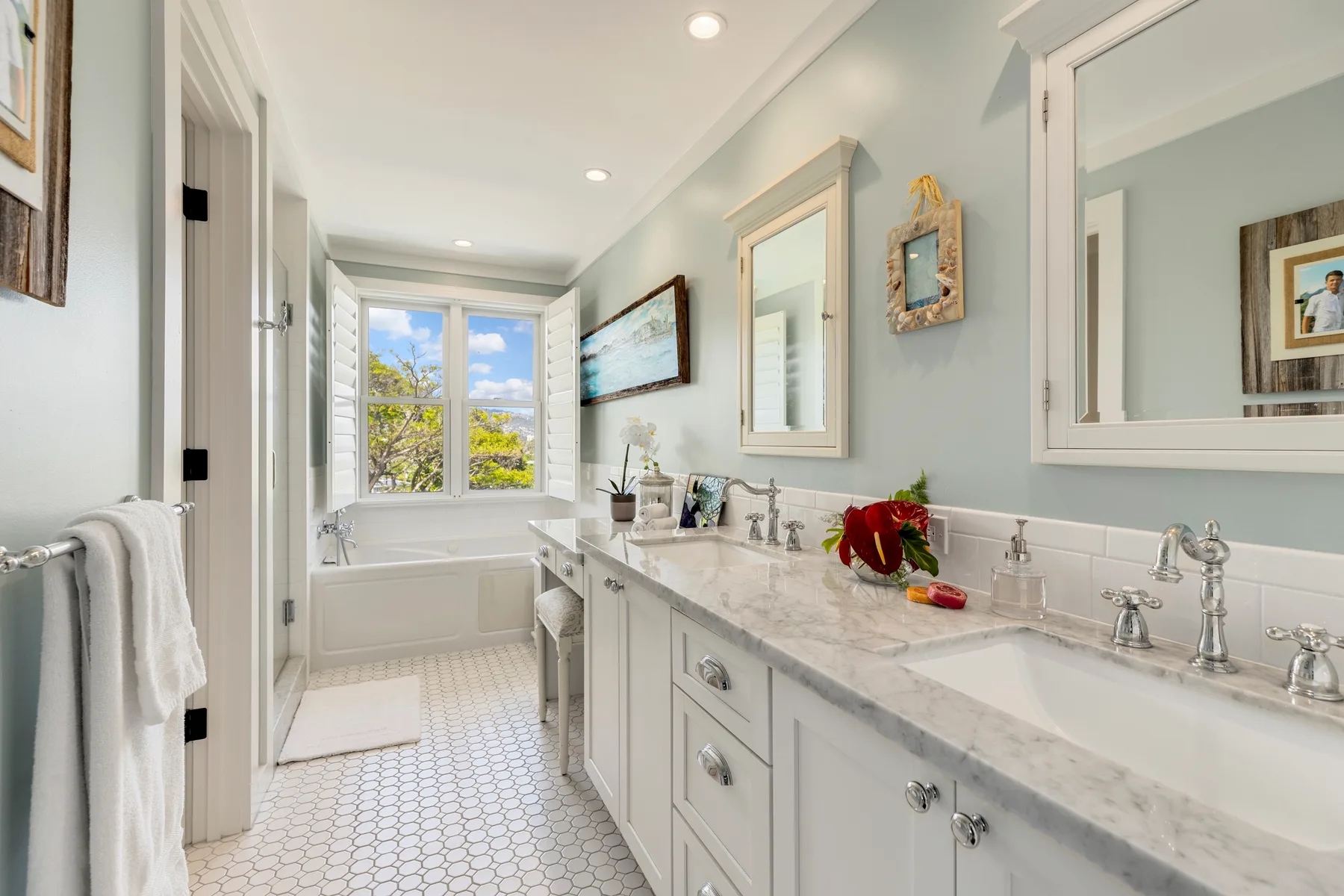 A bright bathroom with a long vanity, mirrors, and a bathtub beneath a window.