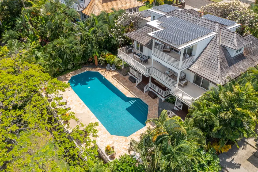Aerial view of a house beside a swimming pool, surrounded by lush greenery.