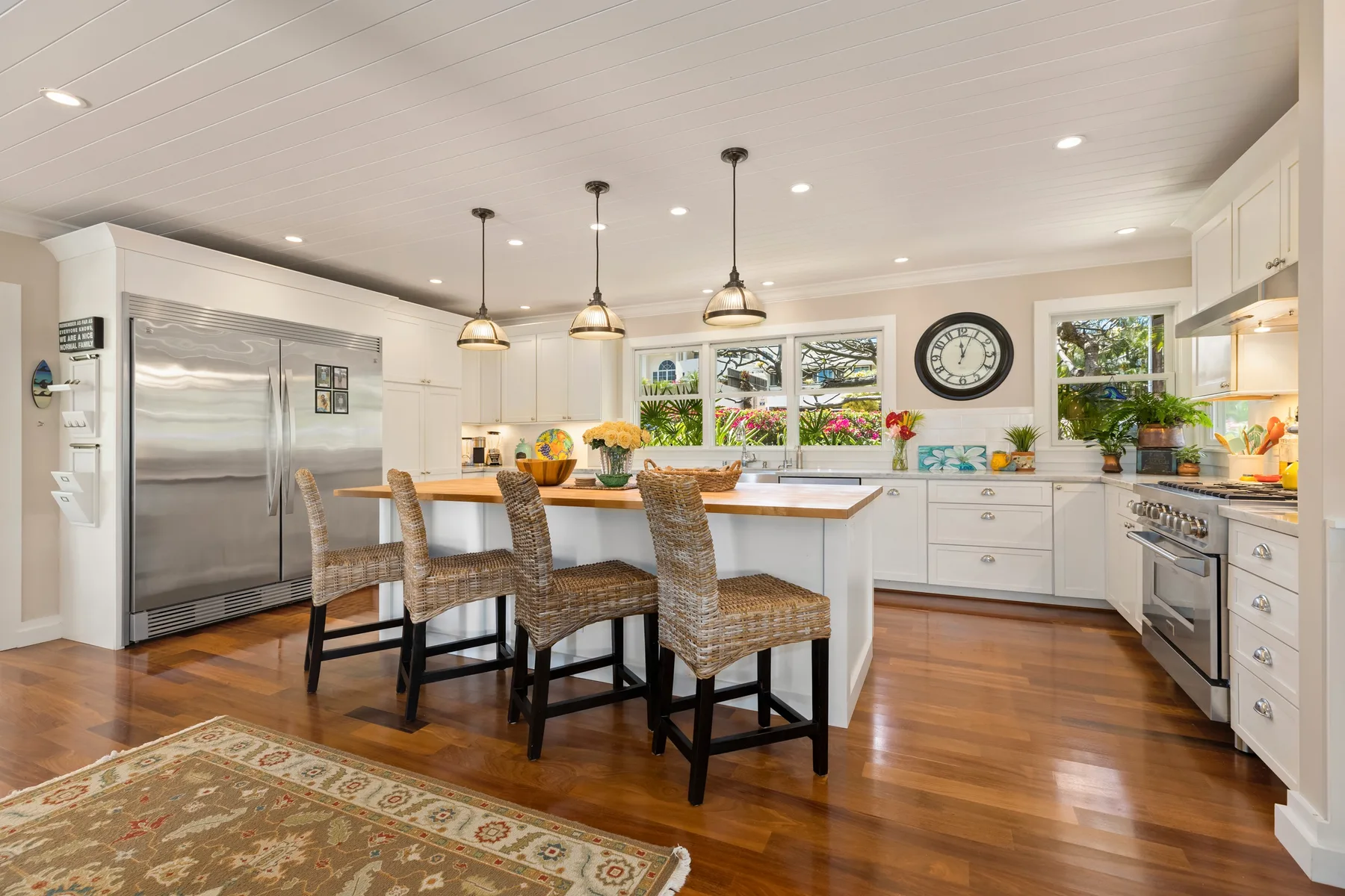A bright kitchen with a central island, woven seating, and stainless steel appliances.