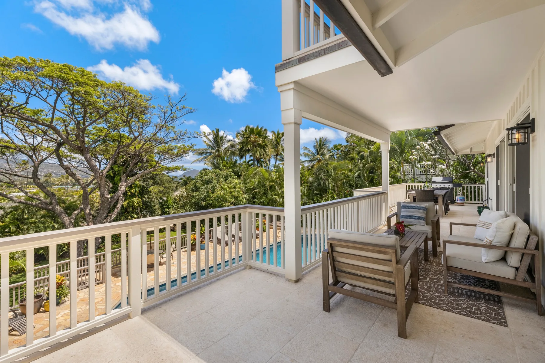 A covered patio with seating overlooks a swimming pool and tropical greenery.