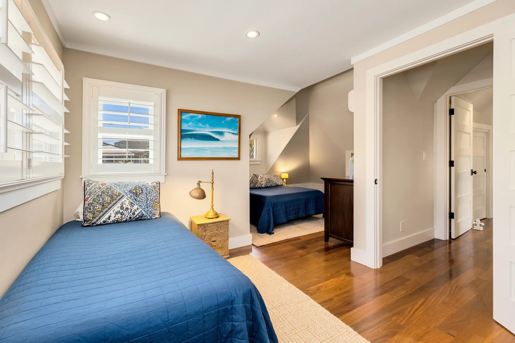 A bedroom with blue bedding, a window, and a second bed in an alcove.