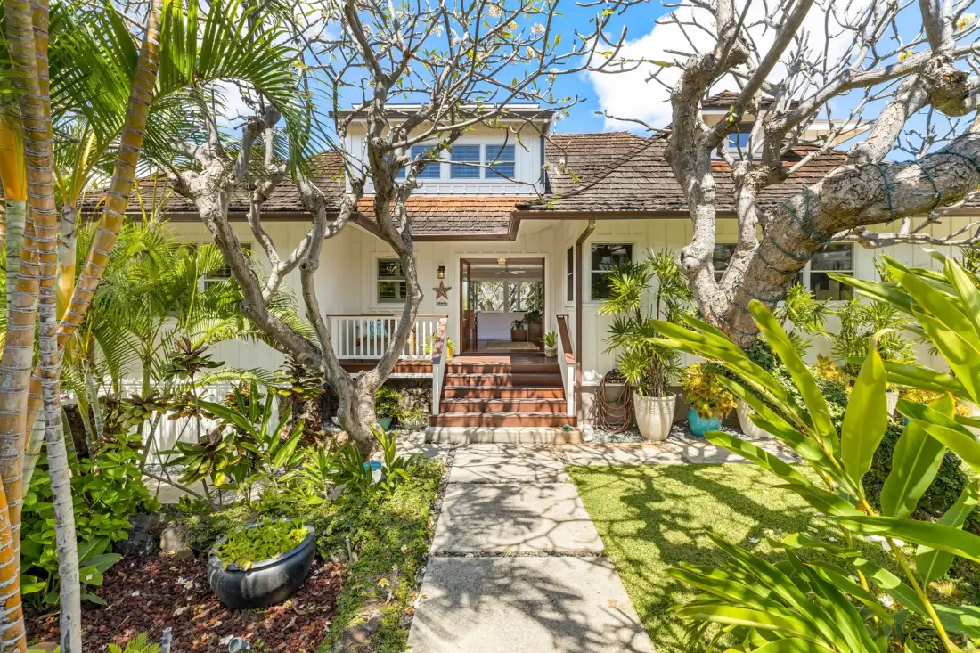 A house entrance with a stone path, steps, and tropical garden plants.