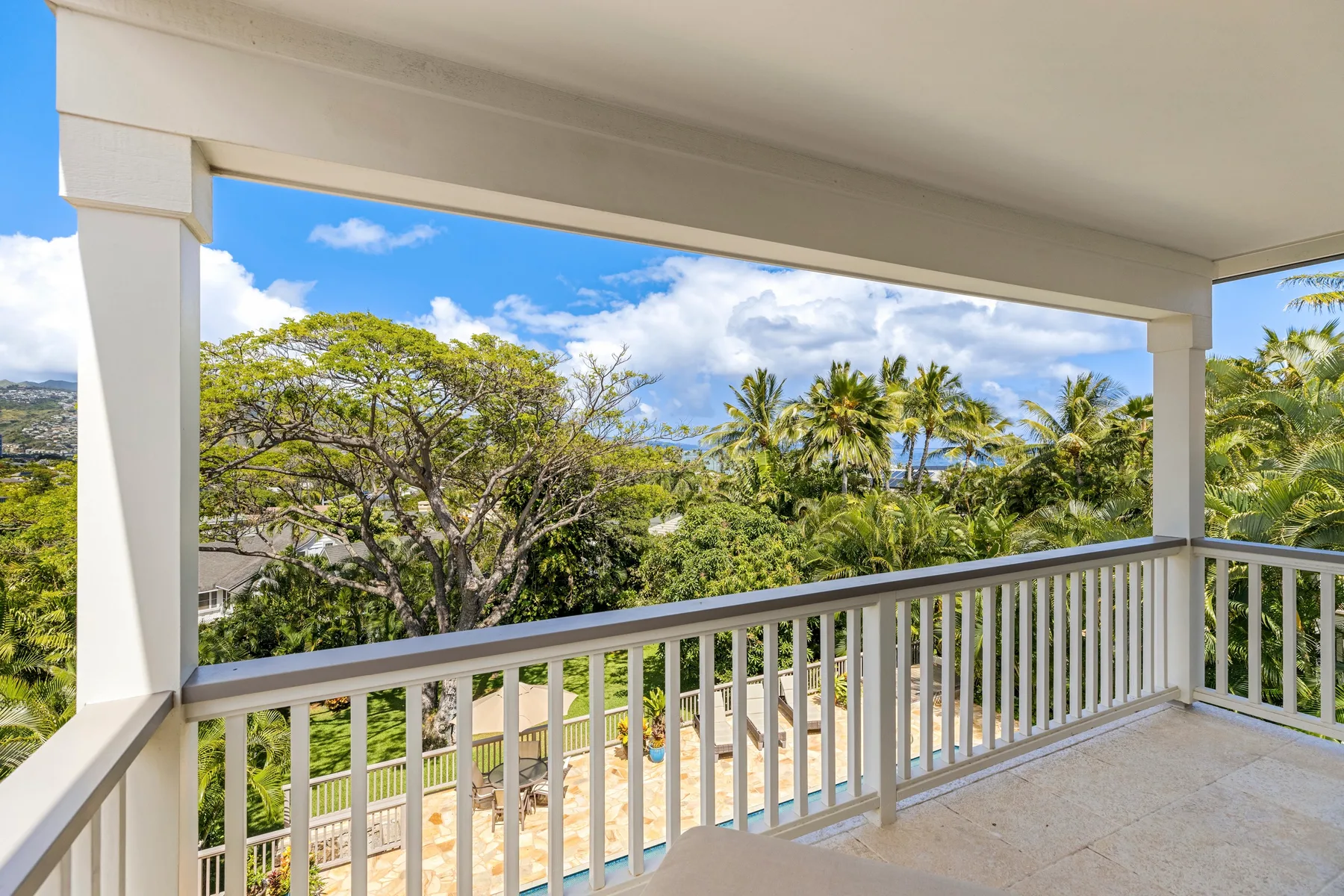 A covered balcony overlooks green trees and a bright blue sky.