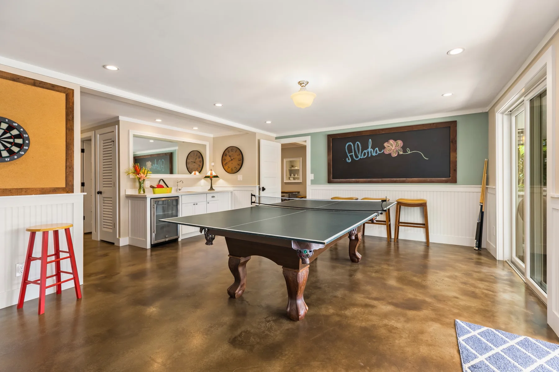 A game room with a pool table, wall-mounted dartboard, and chalkboard.