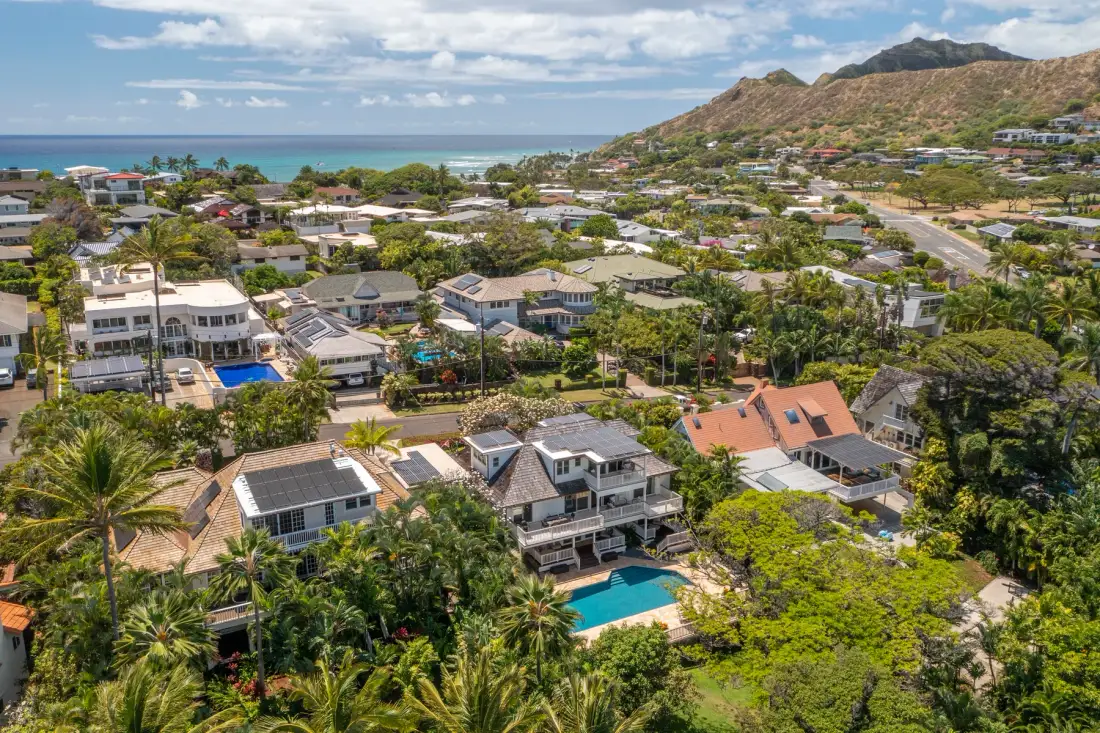 Aerial view of a coastal neighborhood with homes, greenery, and the ocean beyond.
