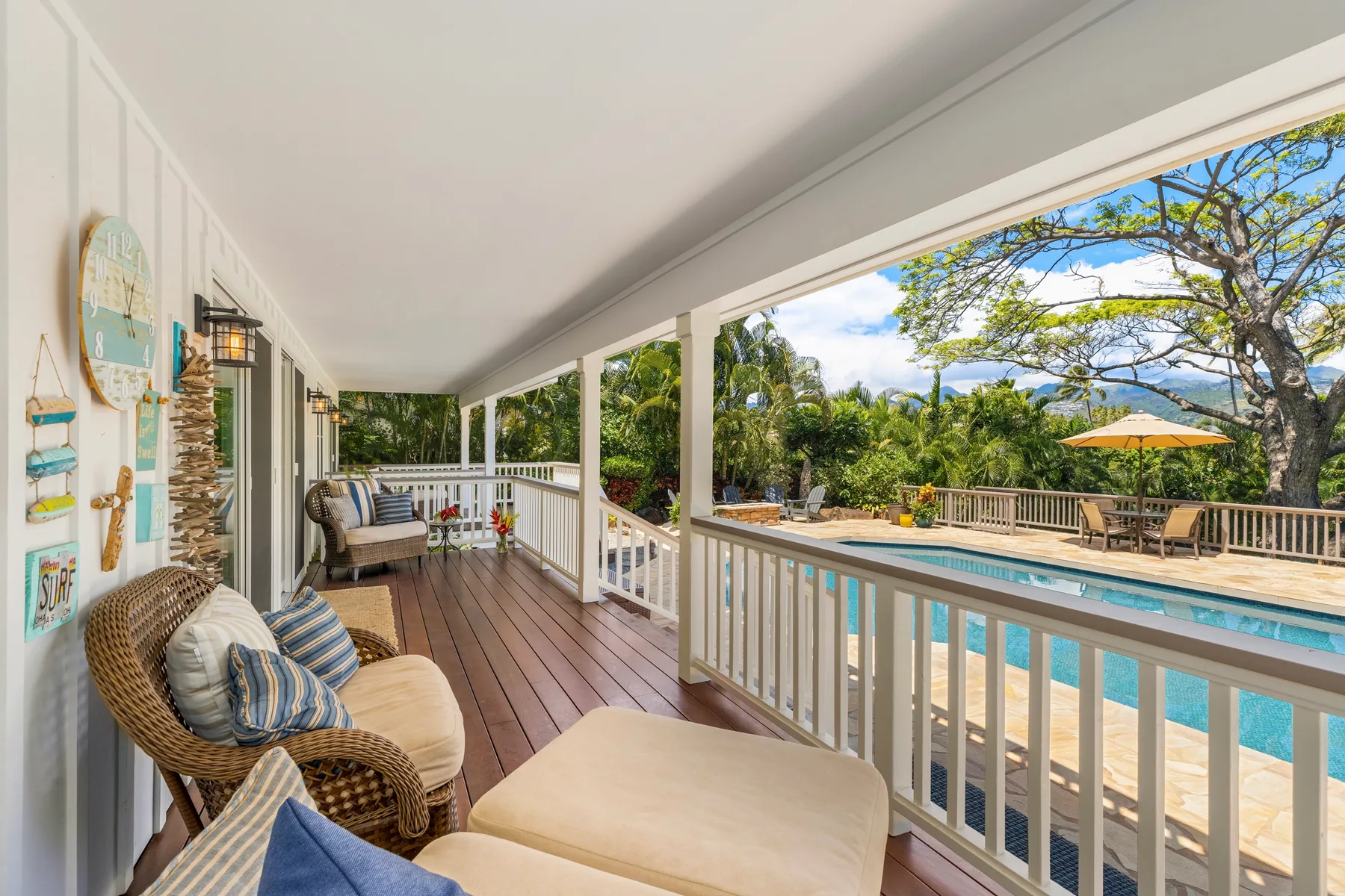 A covered outdoor deck with seating overlooks a swimming pool and garden.