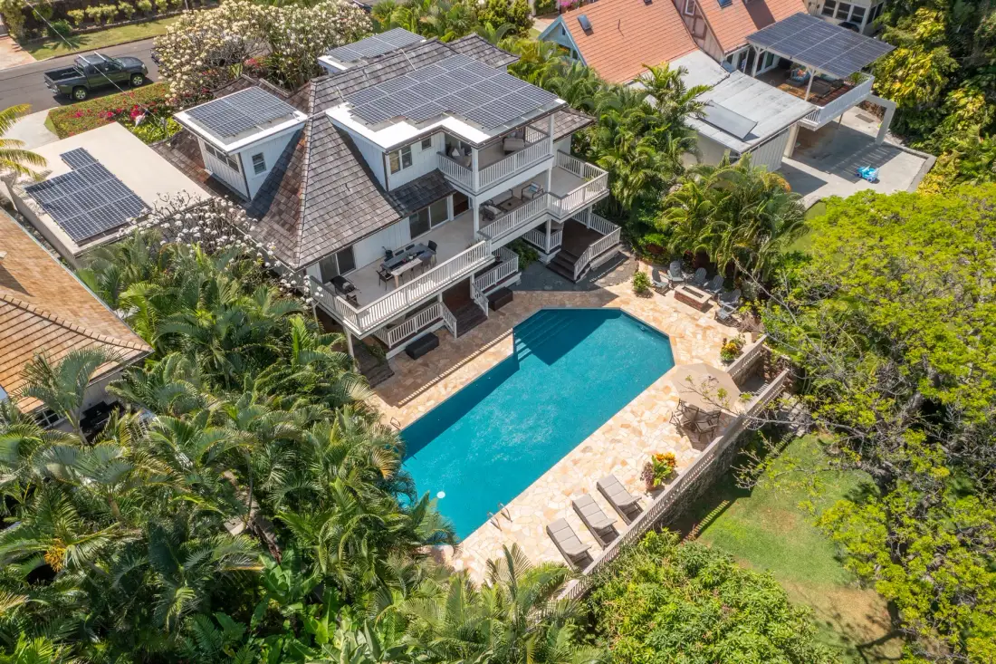 An aerial view of a house beside a swimming pool, surrounded by tropical greenery.