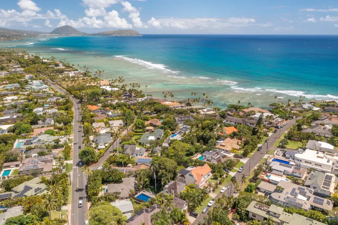 Aerial view of a coastal neighborhood beside turquoise water and a sandy shoreline.
