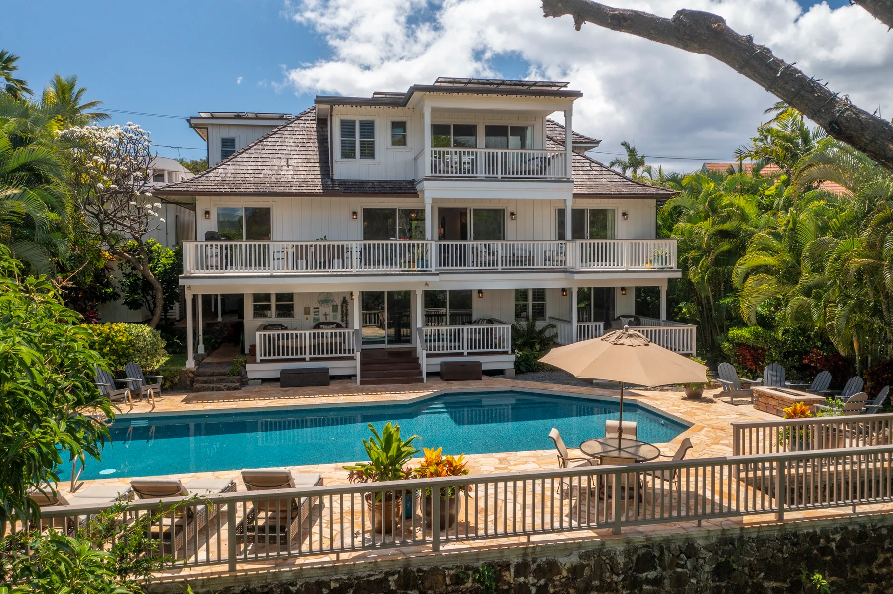 A large house overlooks a swimming pool and surrounding tropical greenery.
