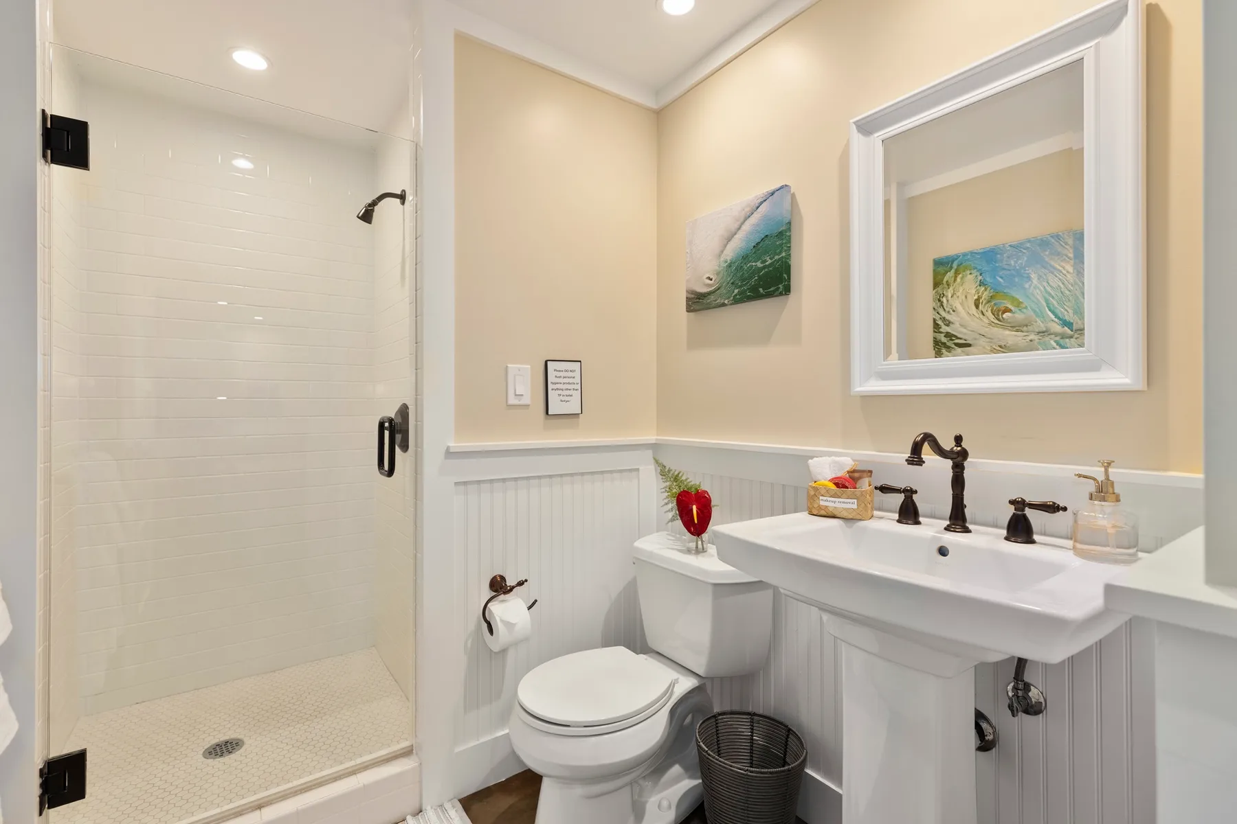 A bathroom with a glass shower, toilet, and sink beneath framed artwork.
