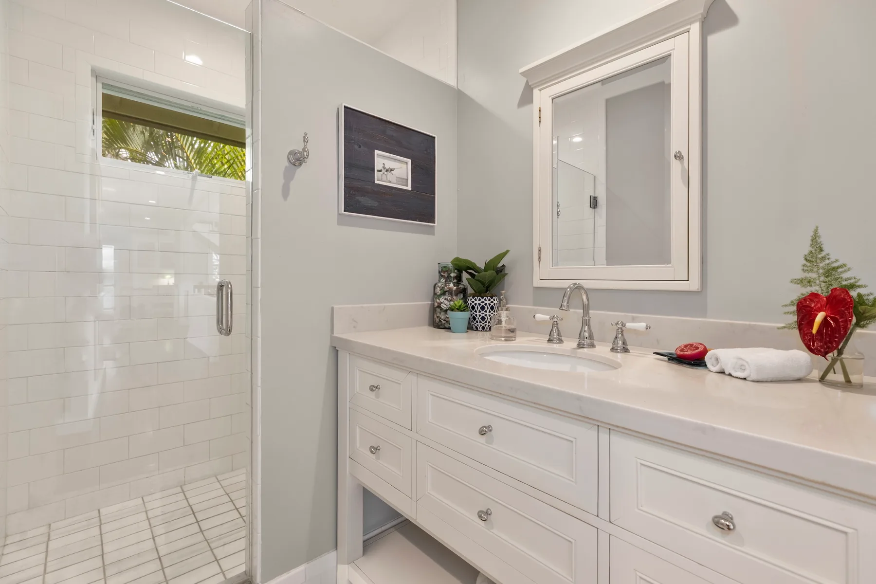 A bright bathroom with a glass shower and a long white vanity.