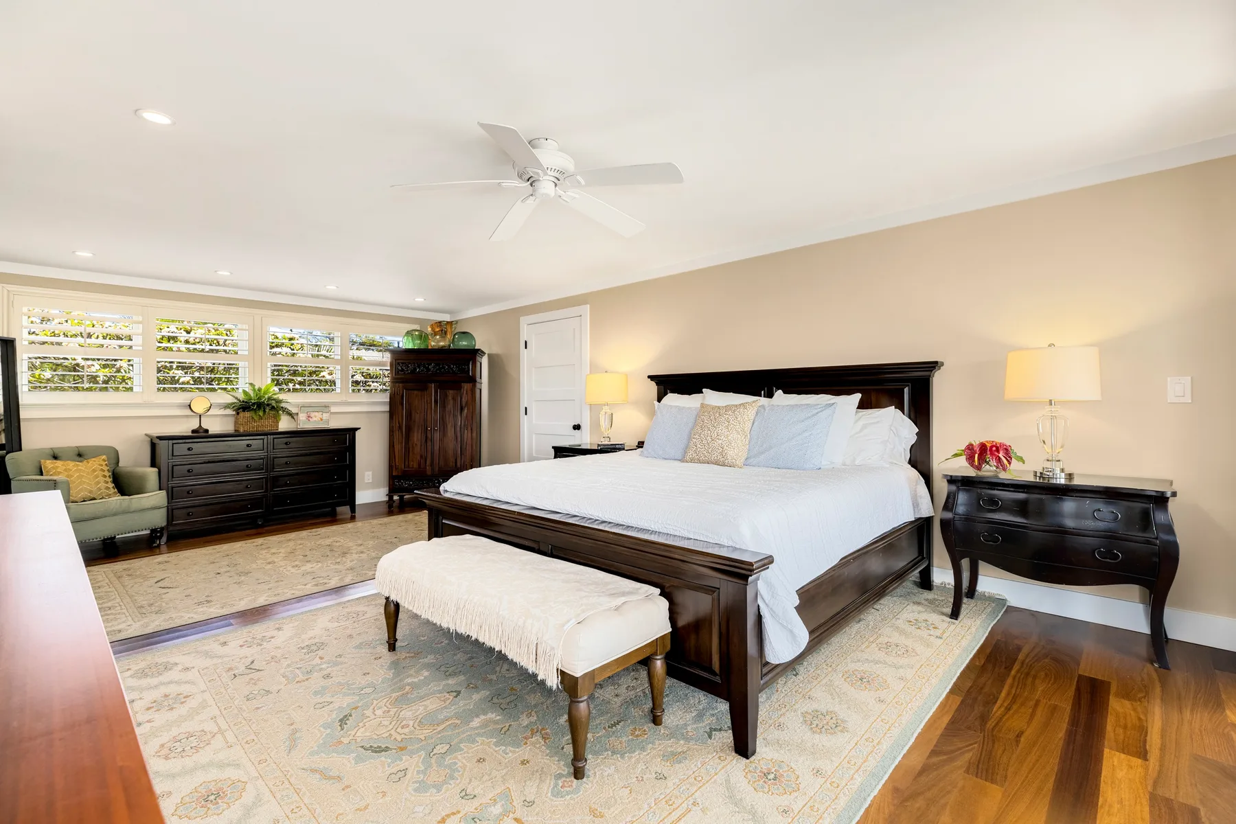 A bright bedroom with a large bed, a bench, and windows along one wall.