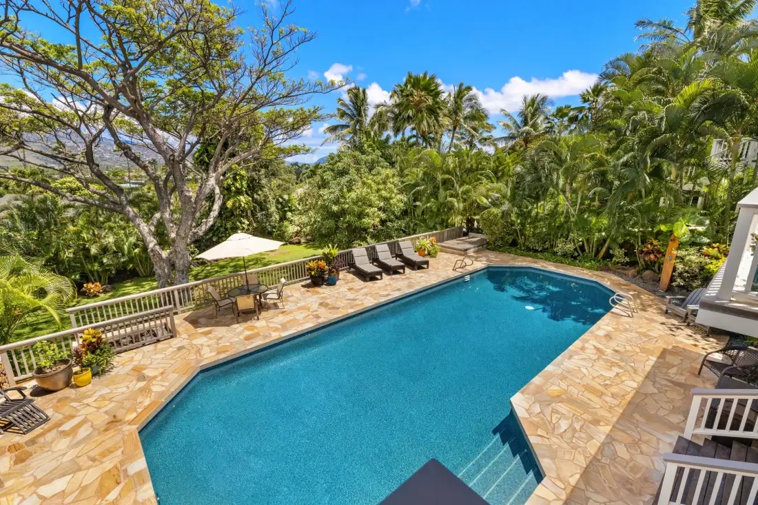 An outdoor swimming pool is surrounded by a stone patio and tropical greenery.