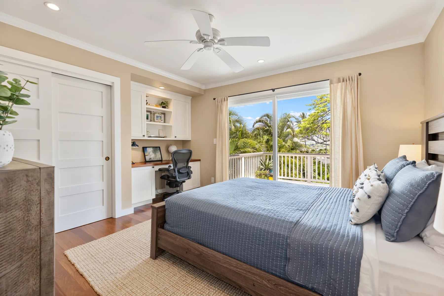 A bright bedroom with a bed beside a wide window overlooking leafy trees.