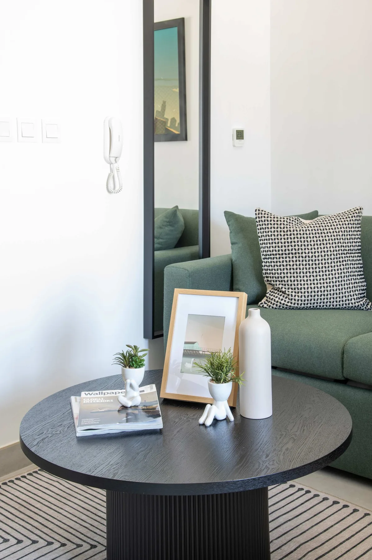 A living room seating area with a green sofa, round coffee table, and framed artwork.