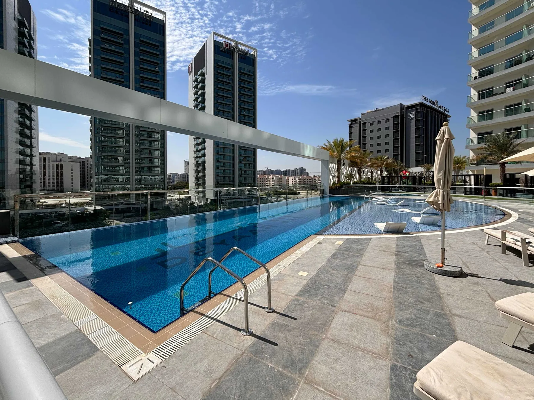 A rooftop swimming pool with lounge seating and high-rise buildings in the background.