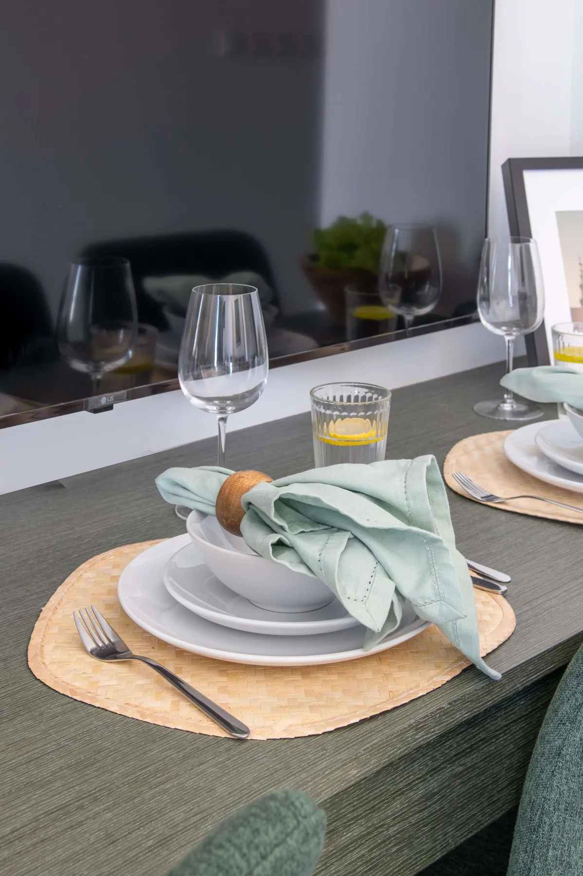 A dining table is set with plates, glasses, and folded napkins.