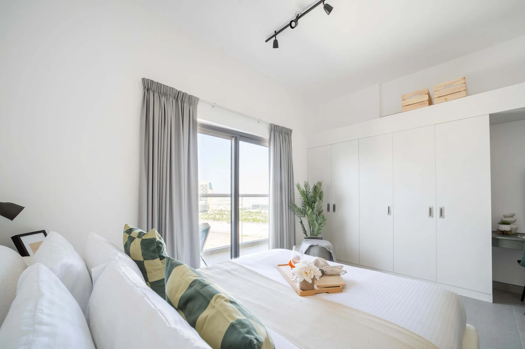 A bright bedroom with a bed beside a large window and built-in wardrobes.