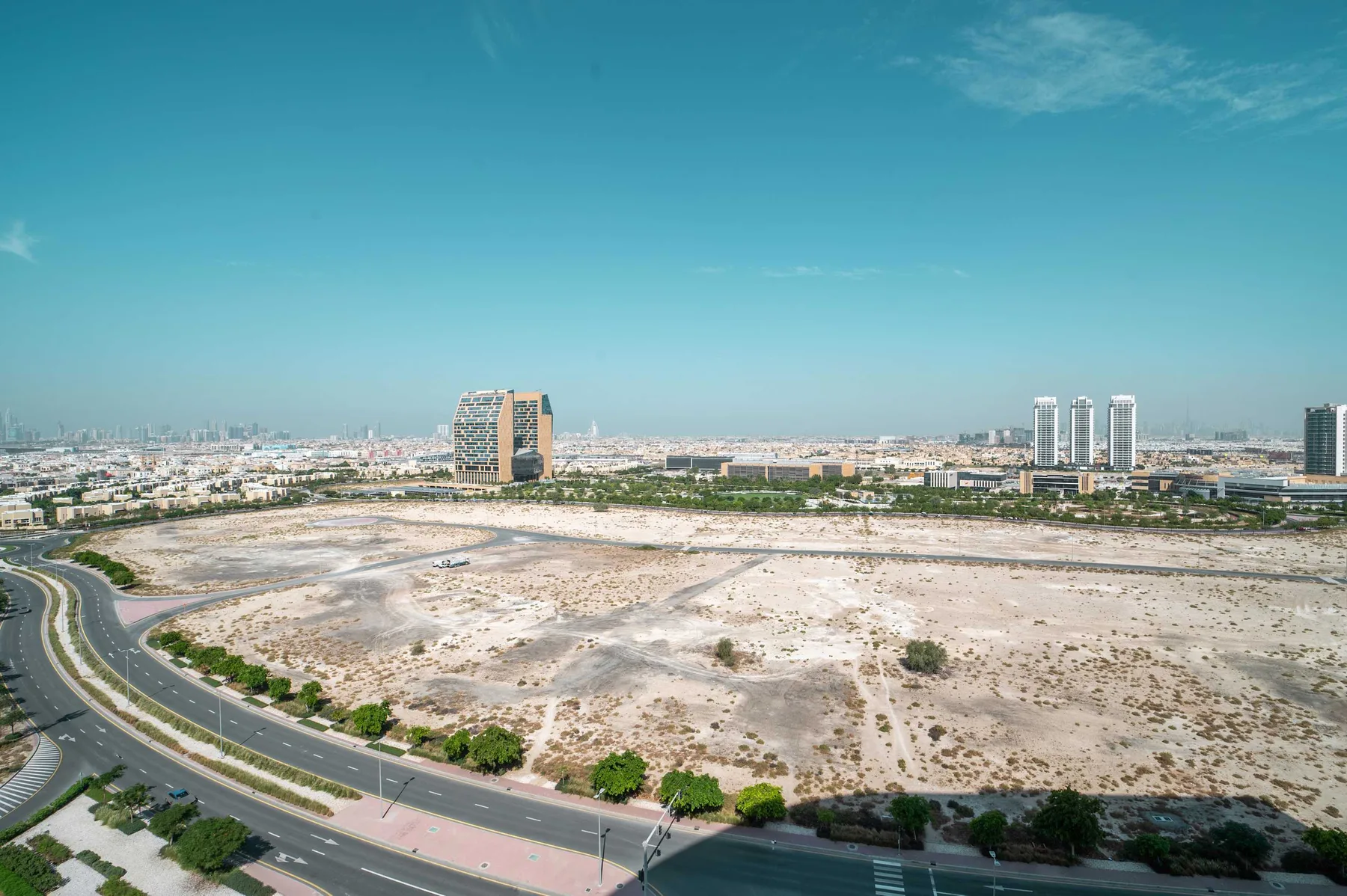 A broad cityscape overlooks a large undeveloped sandy lot and nearby roads.