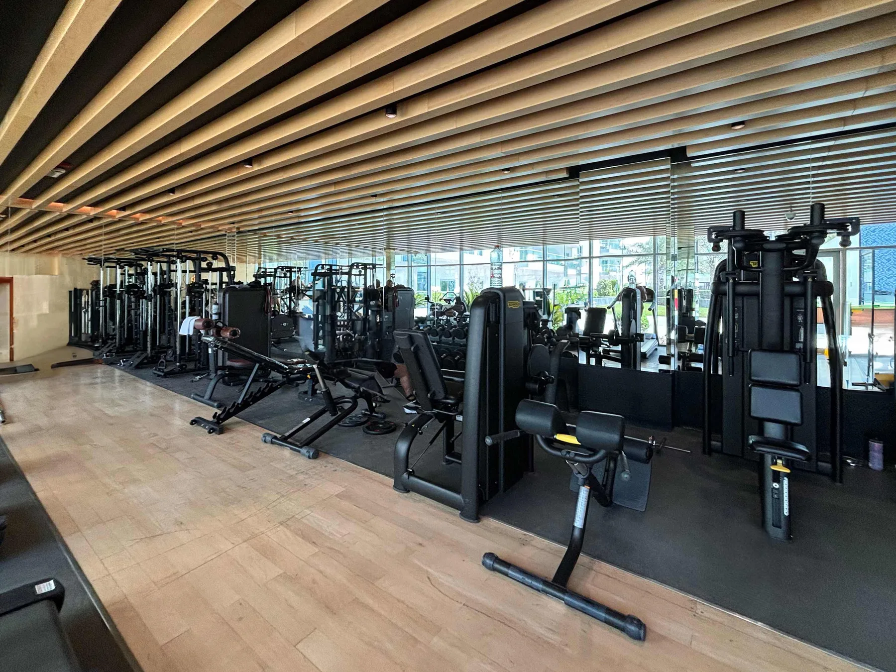 A gym with rows of exercise machines and large windows.