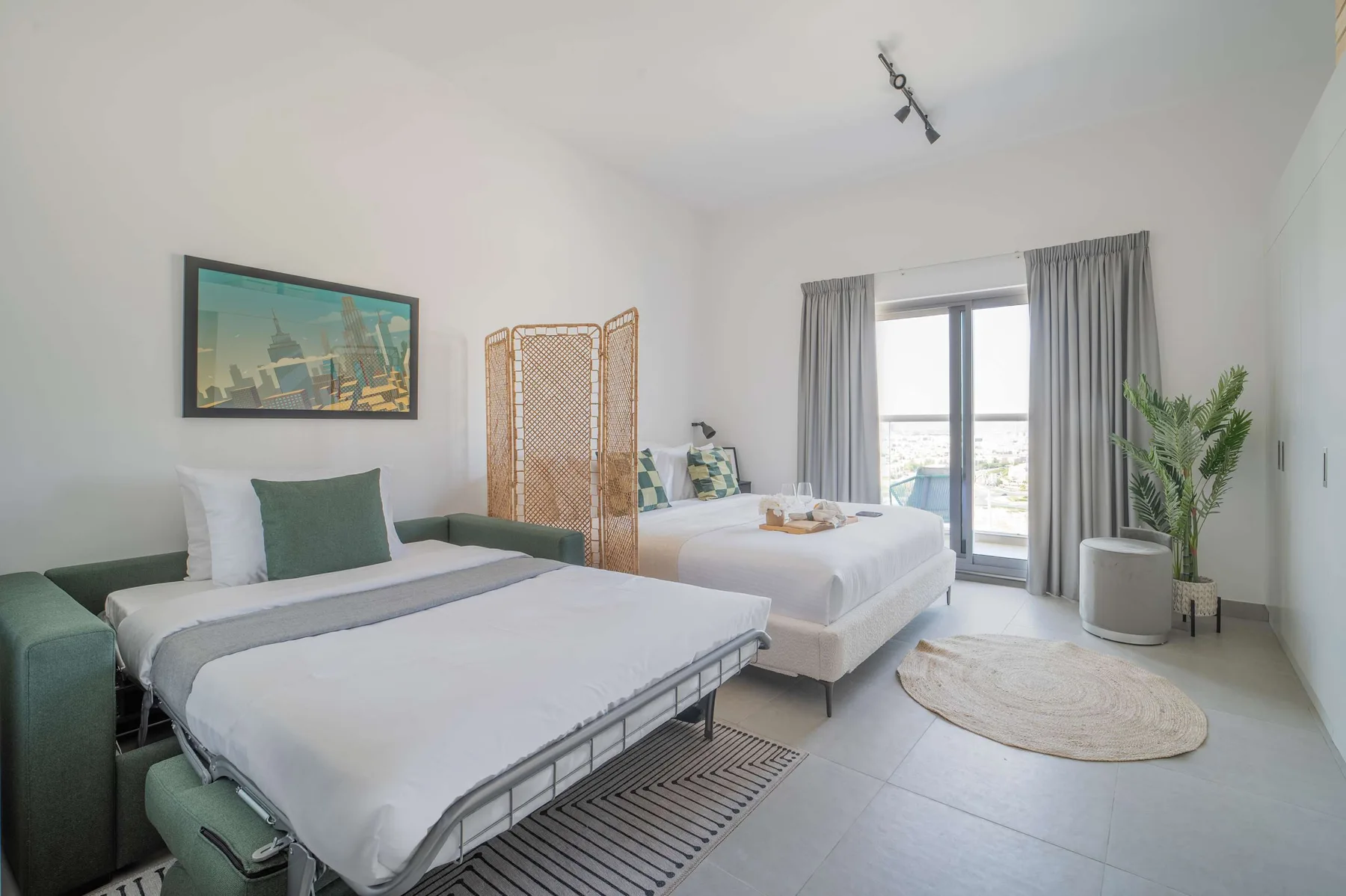 A bright bedroom with two beds and a sliding glass door opening to a balcony.