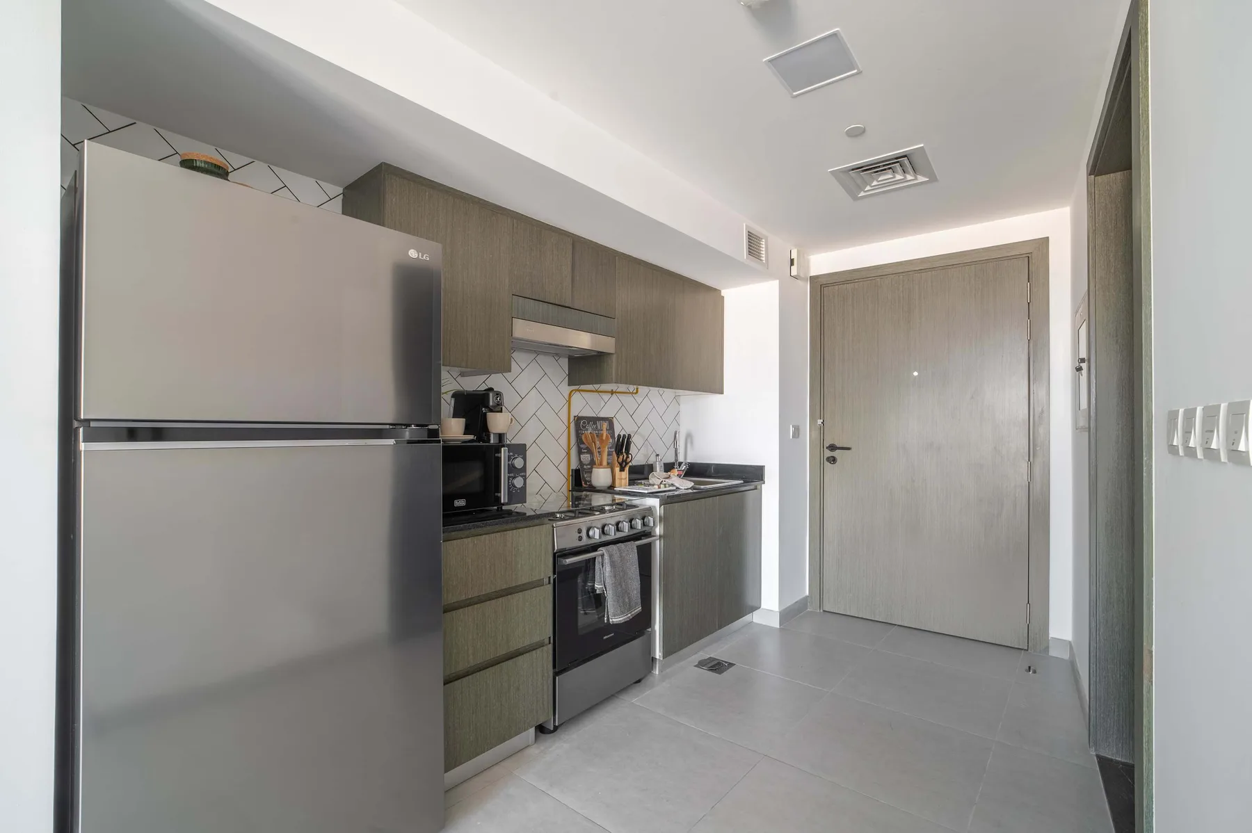 A compact kitchen with a refrigerator, cooktop, and cabinets.