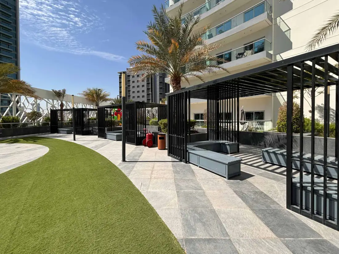 An outdoor courtyard with paved paths, green lawn, and shaded seating.