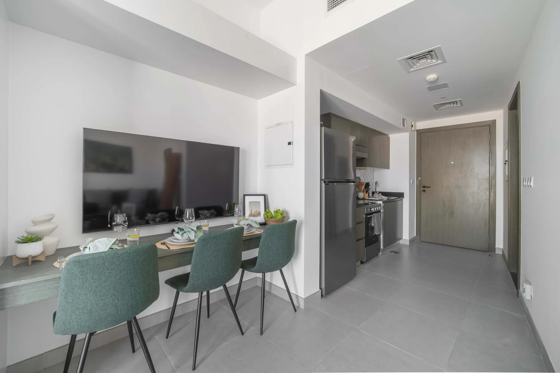 A bright apartment interior with a dining table beside the kitchen and entry hallway.