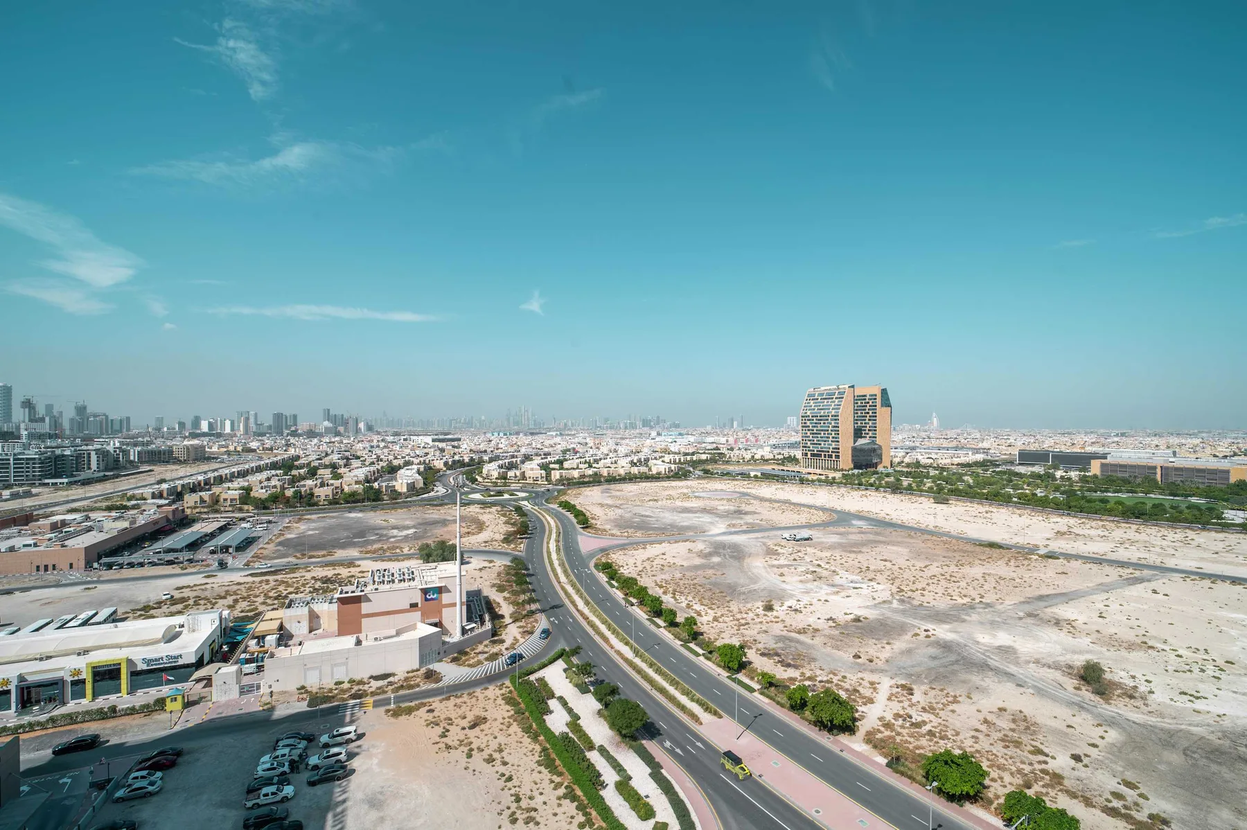 Aerial cityscape with a curving road crossing a broad expanse of open land.