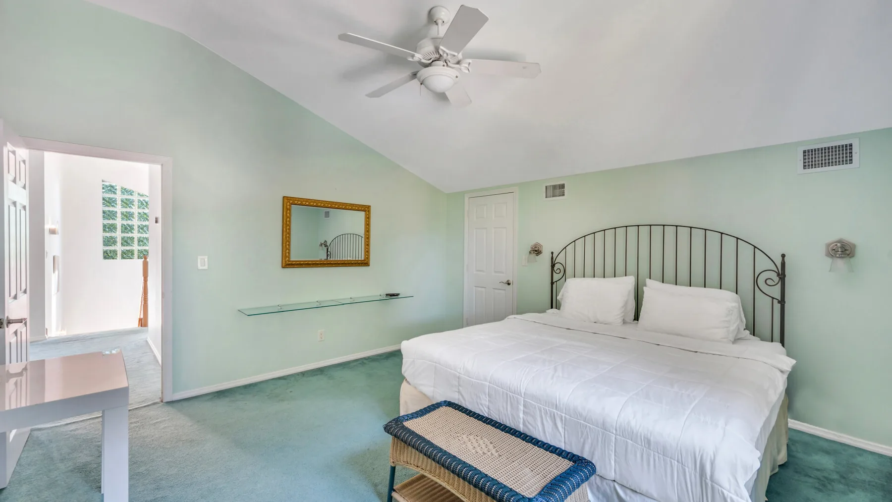 Un dormitorio con una cama grande, paredes verde claro y un ventilador de techo.