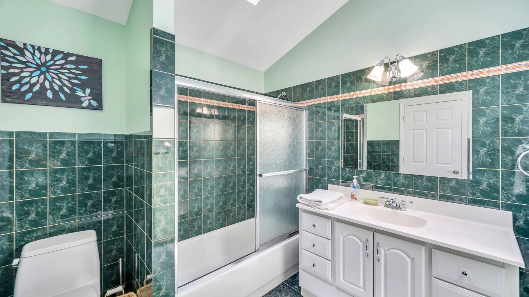 Un baño alicatado con bañera, ducha y tocador blanco.