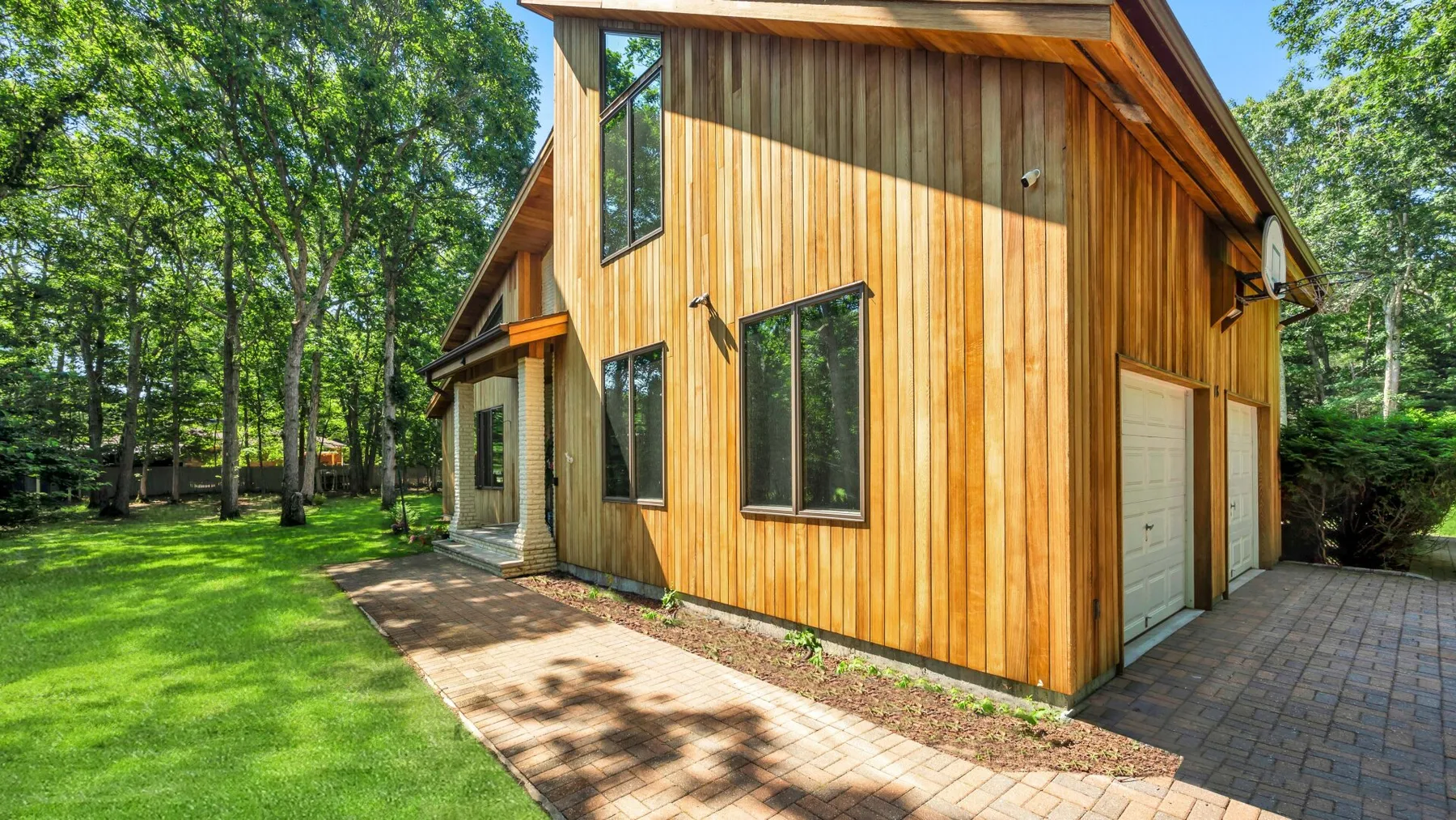 Una casa revestida de madera está junto a una entrada pavimentada y un césped verde.