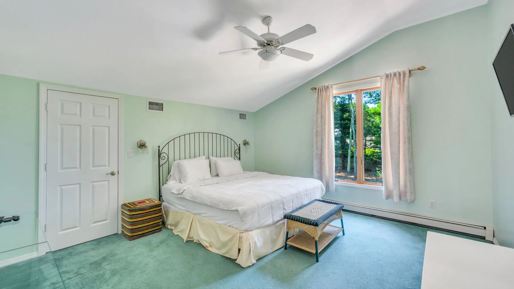 Un dormitorio con una cama, paredes verde pálido y una ventana con cortinas.