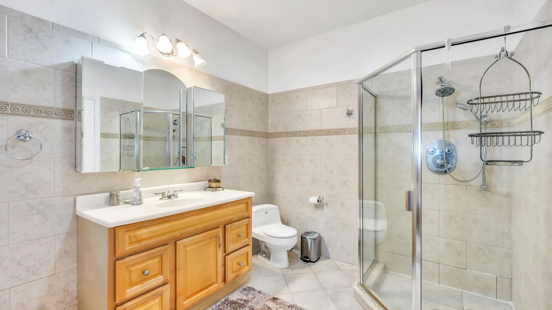 Un baño revestido de azulejos con un mueble de madera y una ducha de vidrio.